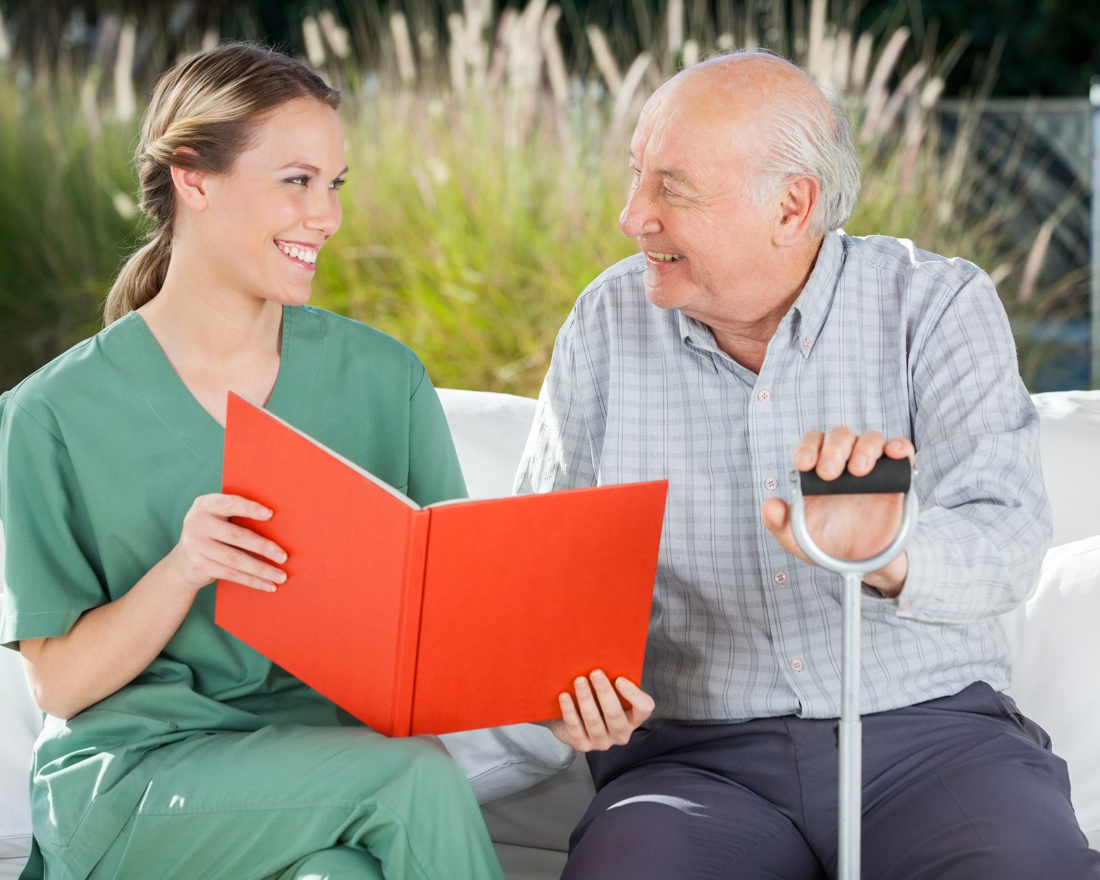 A SteadiCare caregiver reading with an older man on a sunlit porch, both smiling