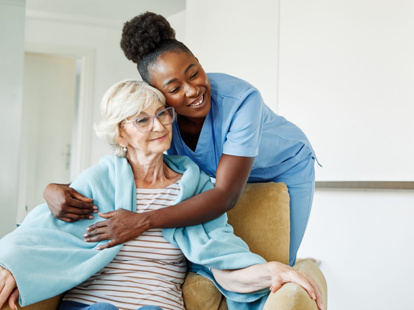 A SteadiCare caregiver warmly embracing a senior woman settled in her armchair
