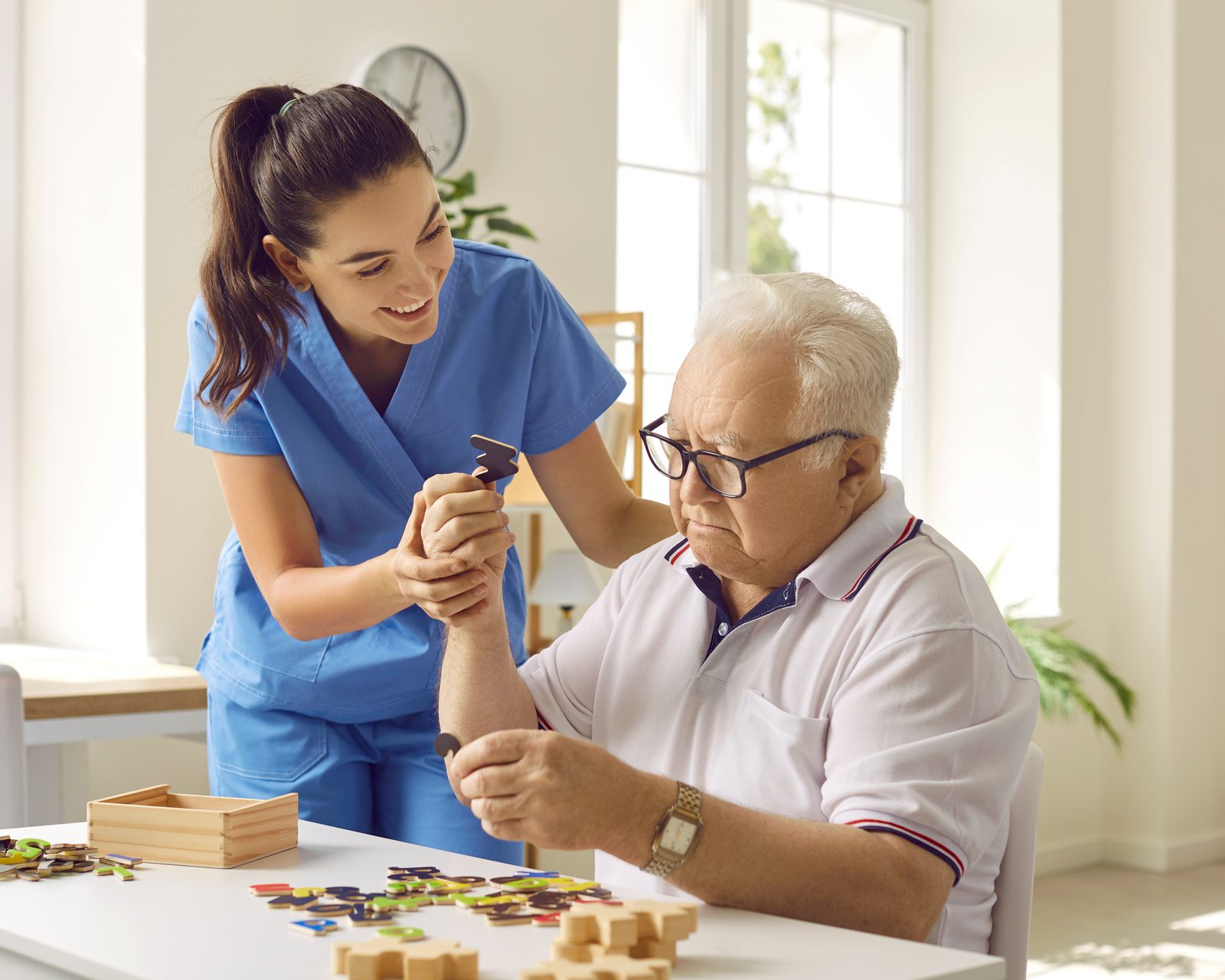 A SteadiCare caregiver gently helping an older man with a word puzzle at his table