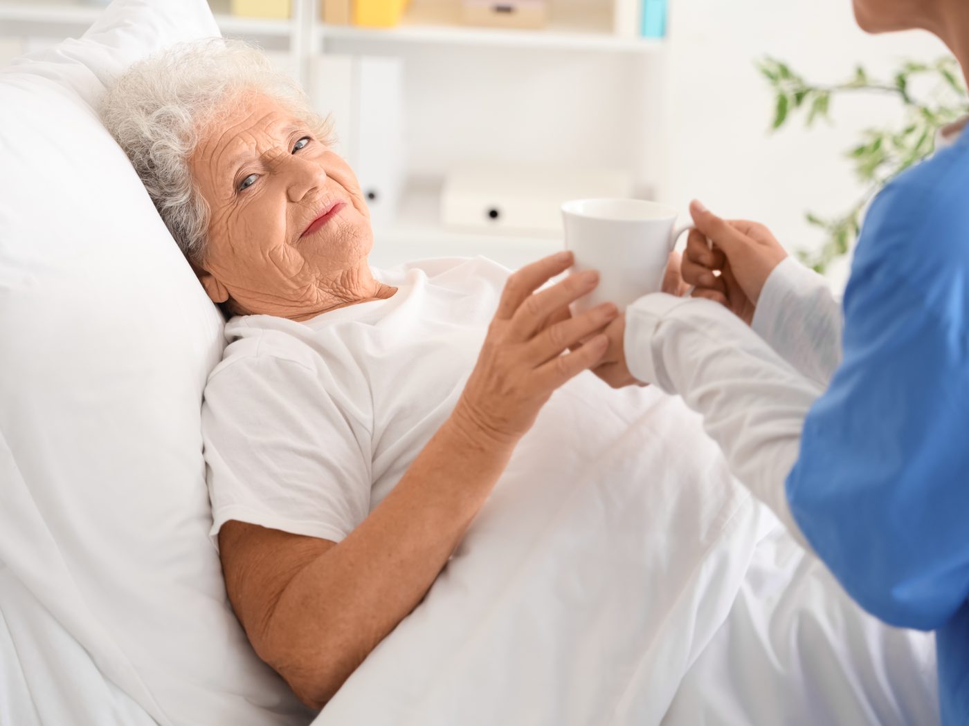 A SteadiCare caregiver bringing a resting senior woman a cup of tea in bed